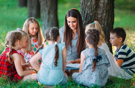 Children and education, young woman at work as educator reading book to boys and girls in park.