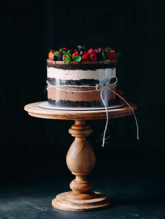 Fruit cake. Cake decorated with berries on a wooden stand on a black background.の写真素材