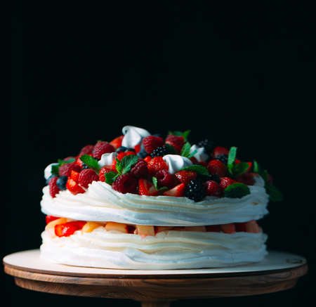 Fruit cake. Cake decorated with berries on a wooden stand on a black background.の写真素材