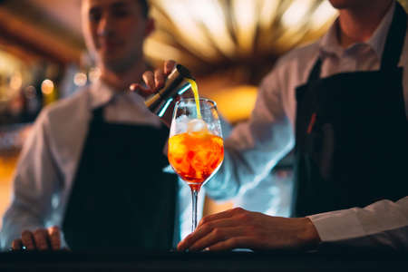 Barman hand stirring a fresh and sweet orange summer cocktail with a spoon on the bar counter.の写真素材