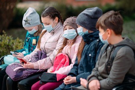 School-age children in medical masks sit on a bench.