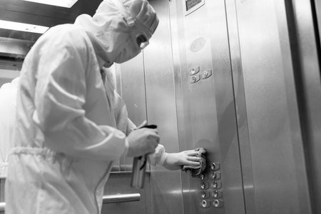 Coronavirus infection. Paramedic in protective mask and costume disinfecting an elevator with sprayer,の写真素材