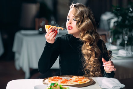 Young beautiful girl alone eating pizza in a restaurant.の写真素材