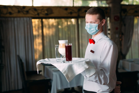 A European-looking waiter in a medical mask serves Latte coffee.