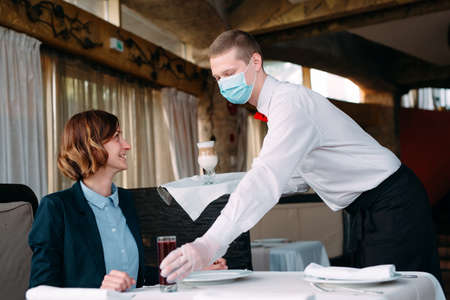 A European-looking waiter in a medical mask serves Latte coffee.の写真素材