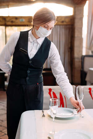 A waiter in a medical protective mask serves the table in the restaurant.の写真素材