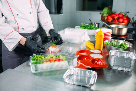 Food delivery in the restaurant. The chef prepares food in the restaurant and packs it in disposable dishes.の写真素材