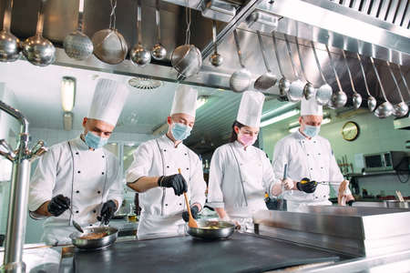 Chefs in protective masks and gloves prepare food in the kitchen of a restaurant or hotel.の写真素材