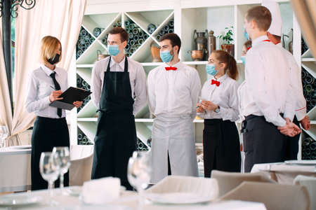 Employees of a Restaurant or Hotel in protective masks. End Of Quarantine. Restaurant Manager and his staff on the terrace. interaction with the chef in the restaurant.の写真素材