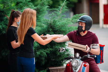 Two womans pick up delivery food box from delivery rider with scooter in front house for social...