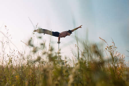 A man of athletic build performs complex gymnastic exercises in a field at sunset.の写真素材