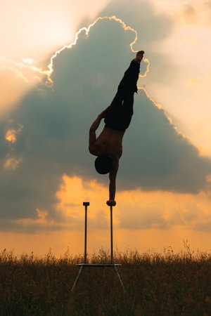 A man of athletic build performs complex gymnastic exercises in a field at sunset.