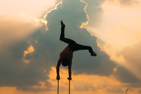 A man of athletic build performs complex gymnastic exercises in a field at sunset.