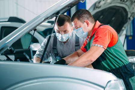 Mechanics in uniform and protective masks work in a car workshop.の写真素材
