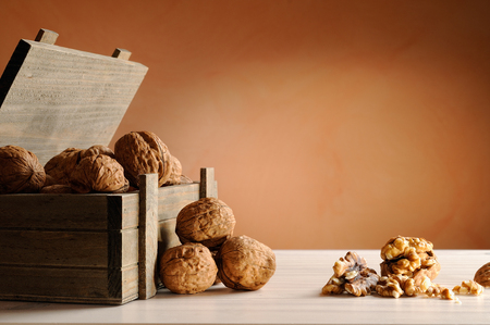 group of walnuts on a white table with trunk wooden container and brown backgroundの写真素材