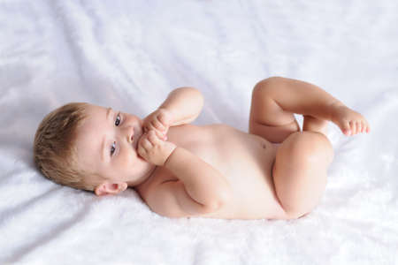 baby biting hands lying on a blanket of white hairの写真素材