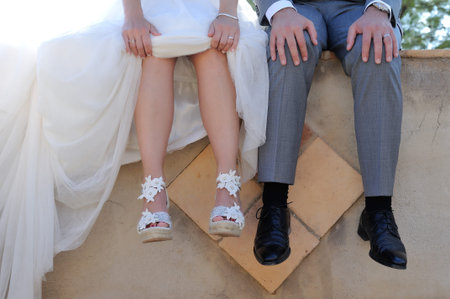 feet of bride and groom sitting on a concrete wall outdoor