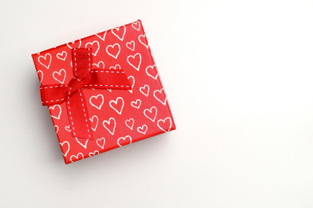 Decorative square red gift box with red ribbon and white painted hearts. Top view. White isolated background.の写真素材