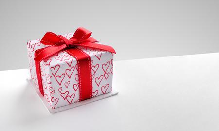 Decorative gift box with red ribbon and hearts printed on white table. Top view left. Grey background. Horizontal composition.の写真素材