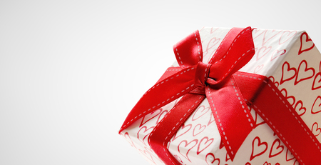 Decorative white gift box with red ribbon and hearts printed close up. Front view. Grey background. Horizontal composition.の写真素材