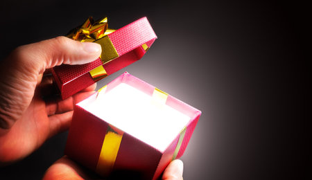 hands opening a red gift box with gold ribbon in shadow. Horizontal composition. Top view.