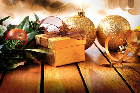 Golden Christmas decoration on a wooden table. With golden gift box, two golden balls and floral ornament with bokeh background with stars. Front view. Horizontal composition.の写真素材
