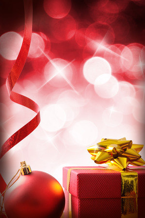 Red Christmas decoration with red gift box and ribbon and ball. Red bokeh background with stars. Front view. Vertical composition.の写真素材