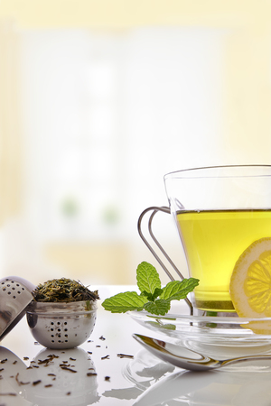 Glass cup green tea with mint and lemon, and strainer tea on a table in the living room. Vertical composition. Front view.の写真素材