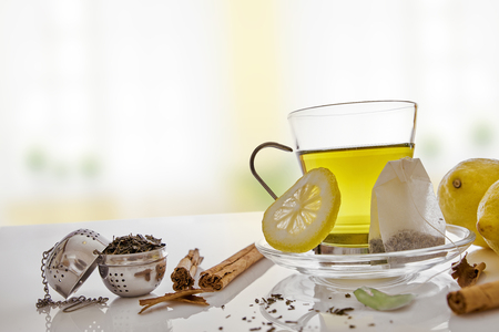 Glass cup green tea with cinnamon stick and lemon on a table in the living room. With teabag and metallic strainer Horizontal composition. Front view.の写真素材