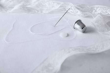 Threading needle thread, thimble and buttons on white fabric and lace decor. Horizontal composition....