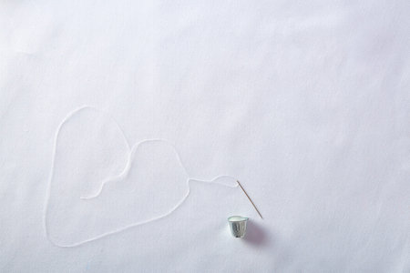 Threading needle thread forming a heart background on white cloth. Horizontal composition. Top view.