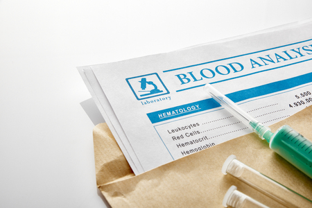 Blood test report in a brown envelope with vials and syringe over white glass table. Horizontal composition. Elevated view.の写真素材