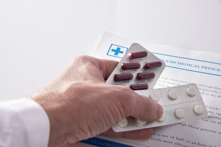 Doctor prescribing drugs with documents and medicines on a white glass table.の写真素材