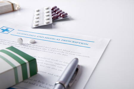 Guidelines and medical prescription with drug blisters on a white glass table.の写真素材