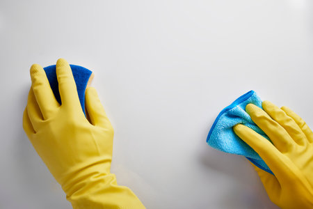 Hands of cleaning staff with rag and scourer working on white table. Top view. Horizontal...