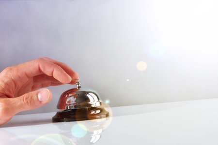 Hand of a Customer ringing the bell hotel service on a table white glass. Concept hotel, travel,...