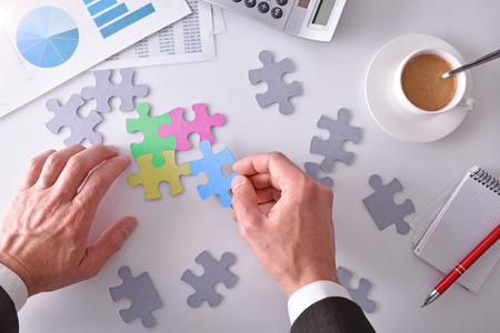Representation and concept of problem solving and project development business. Office table with hands of businessman solving a puzzle.の写真素材