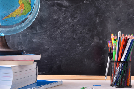 Writing desk with school tools on wood table and blackboard in the background with place in the center for title. Front viewの写真素材