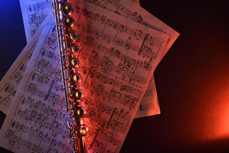 Transverse flute and old sheet music on black table red blue illuminated. Horizontal composition. Top viewの写真素材