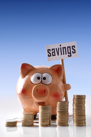 Concept savings with piggy bank with savings billboard and stacked coins on reflective white glass table and blue gradient background. Vertical composition. Front view.の写真素材