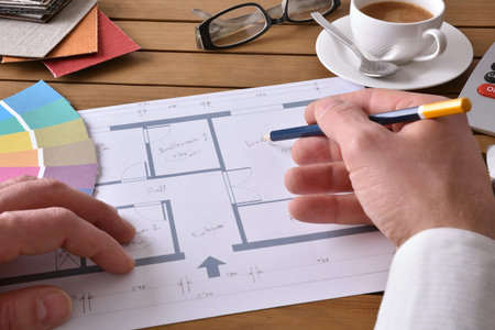 Designer working on an interior design project on wood table with a house plan, tools and samples....