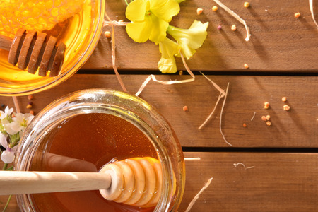 Jar of honey and honeycomb in a glass bowl on a wooden brown table with flowers and bee pollen. Top view. Horizontal compositionの写真素材