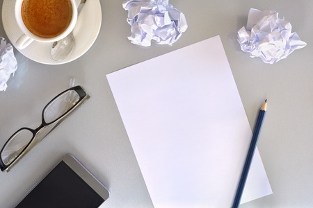 Concept search for ideas in business. Blank sheet on gray office table with crumpled sheets, coffee, glasses and mobile in the background. Top view. Horizontal compositionの写真素材