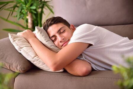 Man napping happily lying on a couch clinging to cushions at home. Front viewの写真素材
