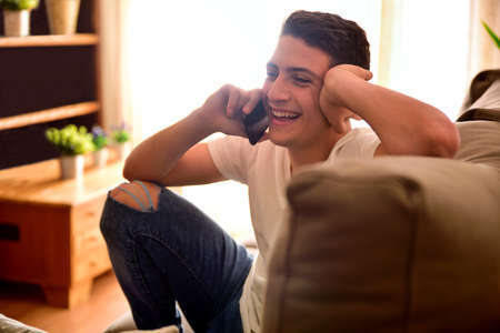 Young boy laughing sitting on couch having a conversation over the phone in the living room close upの写真素材
