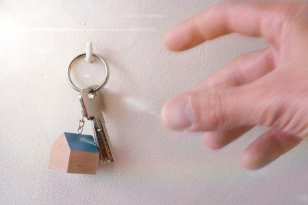 Hands that are going to take keys from a house hung on a hook in the wallの写真素材