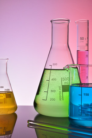 Laboratory glass chemical containers on glass table isolated colorful. Vertical composition. Front viewの写真素材