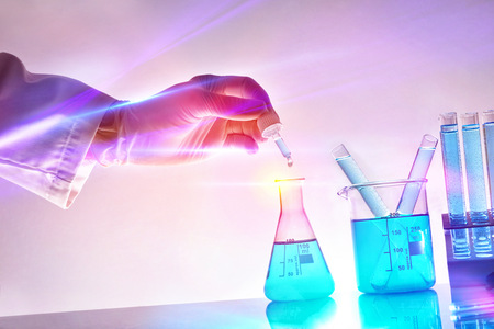 Hand of researcher with dropper and chemical containers with blue liquid in the laboratory with red and blue lights.の写真素材