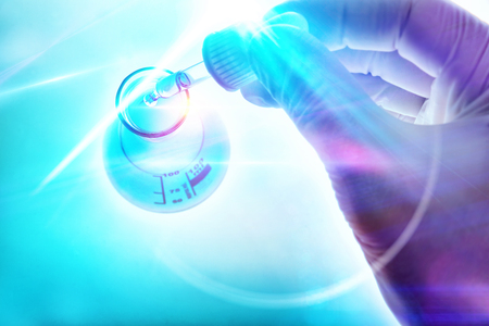 Science and research concept with hand of a scientist with dropper and flask on blue backgroundの写真素材