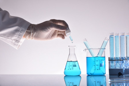 Laboratory worker hand with dropper and glass chemical containers on glass table in the laboratory. Front viewの写真素材